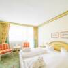 Hotelzimmer im Landhausstil mit Doppelbett, gelben Details und Teppichboden.