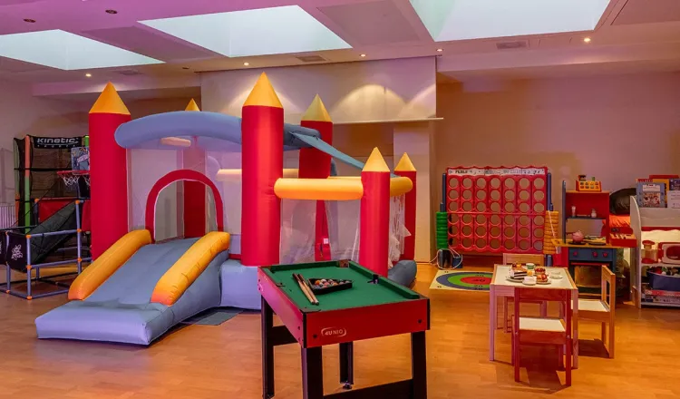 Colourful children's playroom with bouncy castle, children's kitchen, small pool table, table and chairs for creative activities and many other items for child-friendly activities.