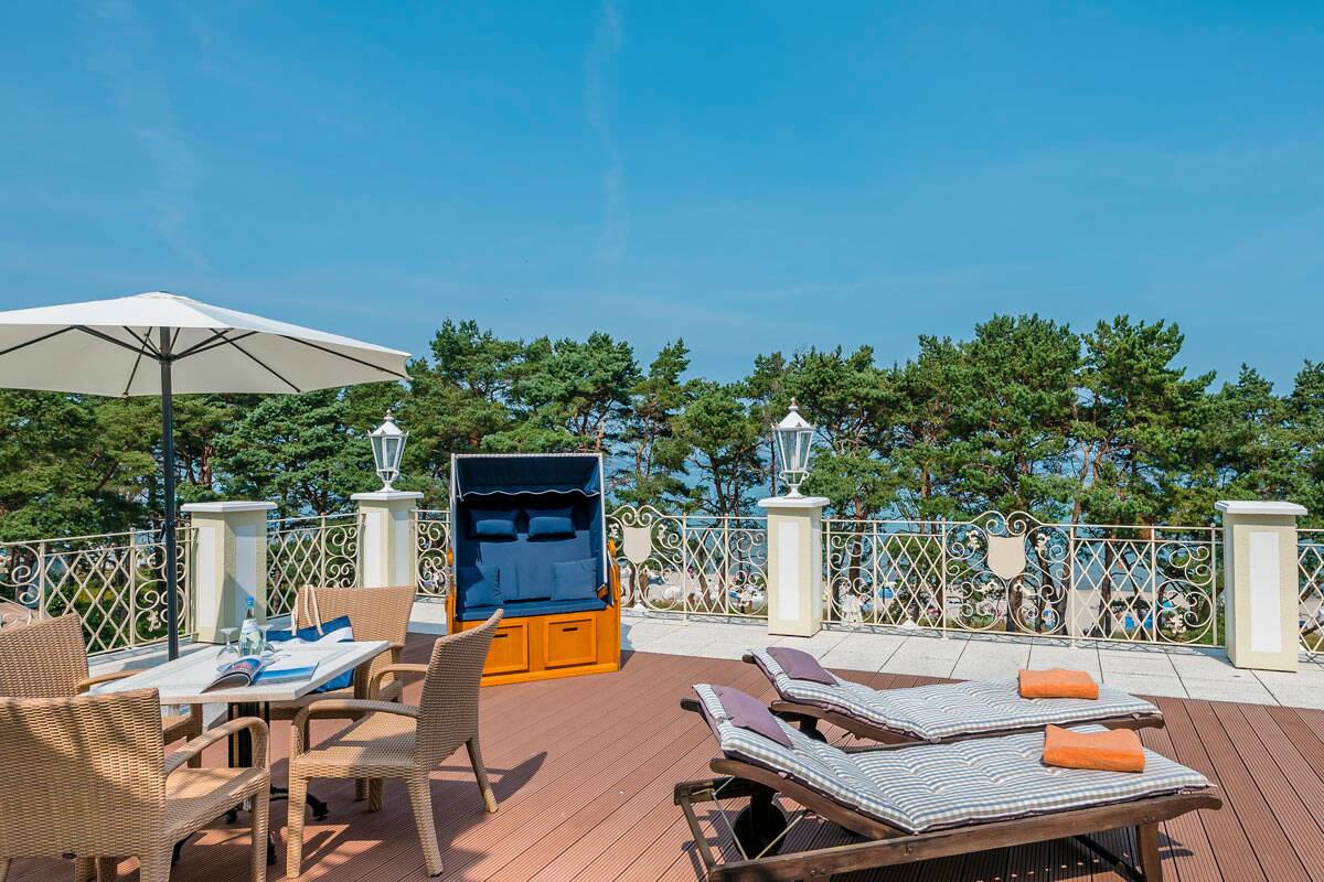 Sonnige Terrasse mit Liegestühlen, Tisch und Strandkorb.
