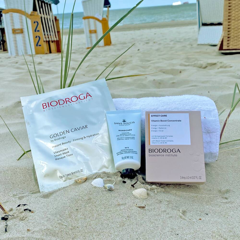 Kosmetikprodukte von Biodroga auf einem Handtuch im Sand.