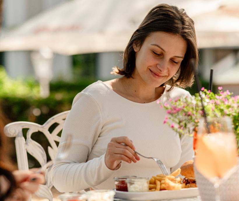 A woman enjoys lunch with fries, a burger, and a drink outdoors in the sunshine on the island of Rügen.