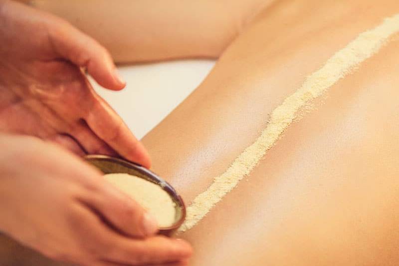 Feines Kräuterpulver, das bei einer Ganzkörpermassage auf einem Rücken verteilt wird.