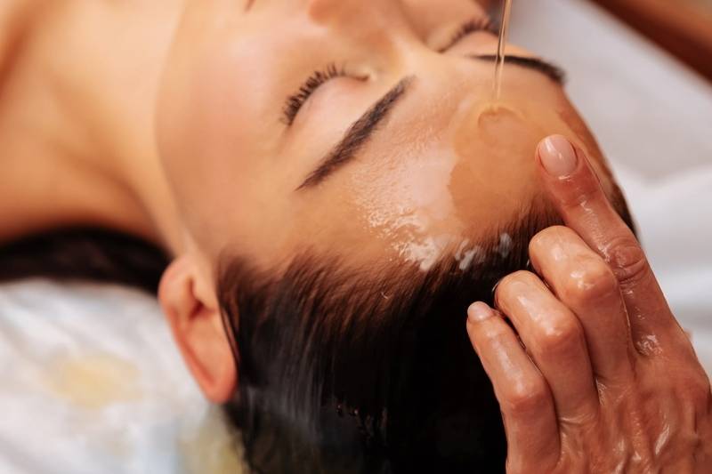 Nahaufnahme einer Frau, der Öl zur Massage auf den Kopf gegossen wird.