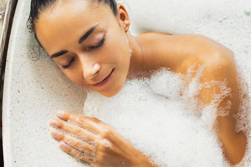 Eine dunkelhaarige Frau nimmt ein Aromaölbad und schließt die Augen, während sie sich entspannt.