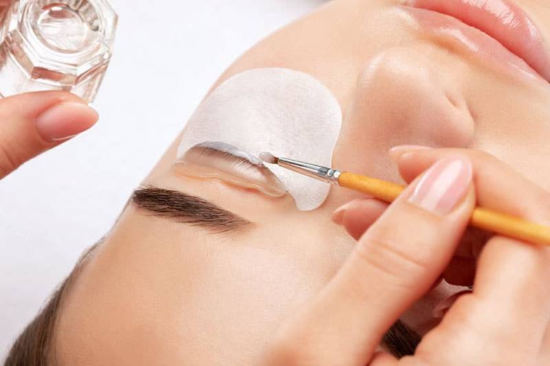 Eine Frau erhält eine Wimpernwelle mit haftender Silikonform und Pinsel.