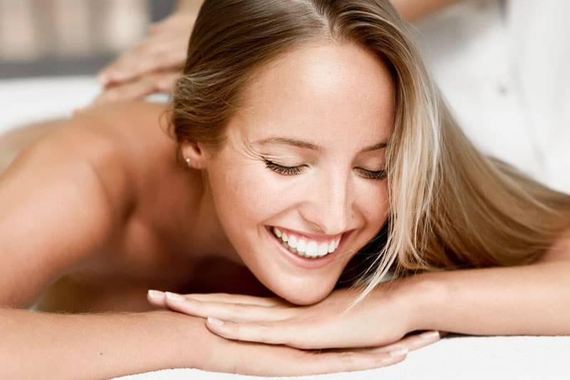 Frau lächelt entspannt, während sie eine Rückenmassage erhält.
