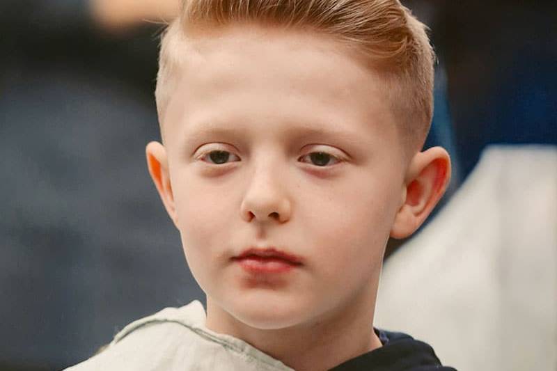 Ein blonder Junge mit Kleiderschutz, neuem Kurzhaarschnitt und Styling.