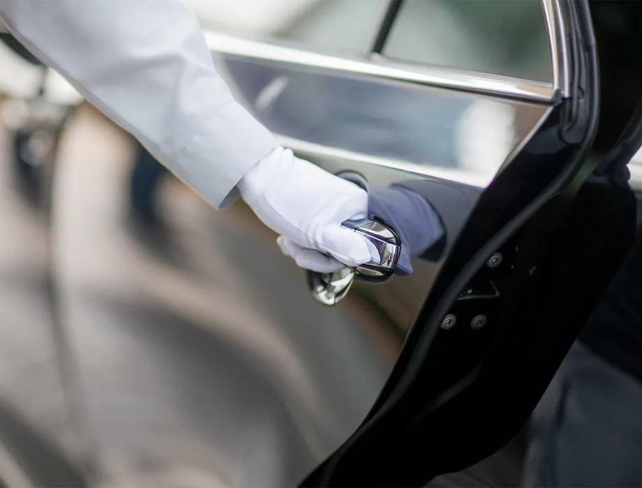 Close-up of the gloved hand of a hotel employee opening a dark car door.