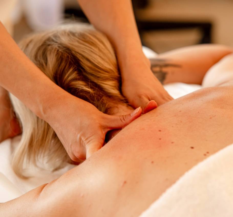 Rückenmassage bei einer Frau mit blonden Haaren, Nahaufnahme der massierenden Hände im Wellnessbereich.