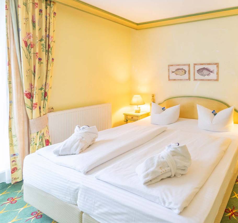 Doppelzimmer im Rugard Strandhotel mit einem großzügigen Doppelbett, dekorativen Kissen und sanfter Beleuchtung.