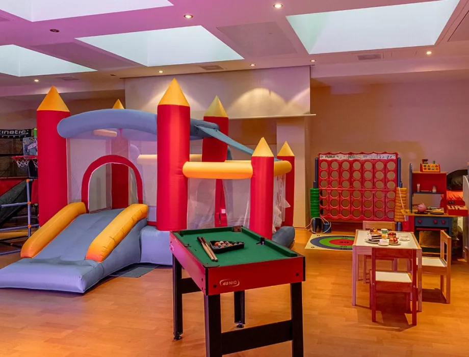 Colourful children's playroom with bouncy castle, children's kitchen, small pool table, table and chairs for creative activities and many other items for child-friendly activities.