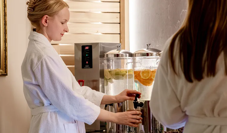 Woman in a bathrobe taps fresh Rügen water with citrus fruits at the spa bar of the Rugard Thermal Strandhotel.