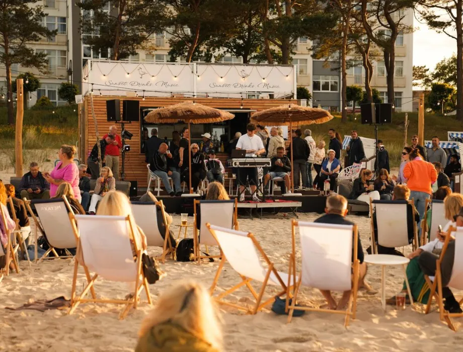 Gäste bei Musik und Drinks am Arkona Beach in Binz mit DJ, Liegestühlen und Sitzplätzen direkt im Sand.