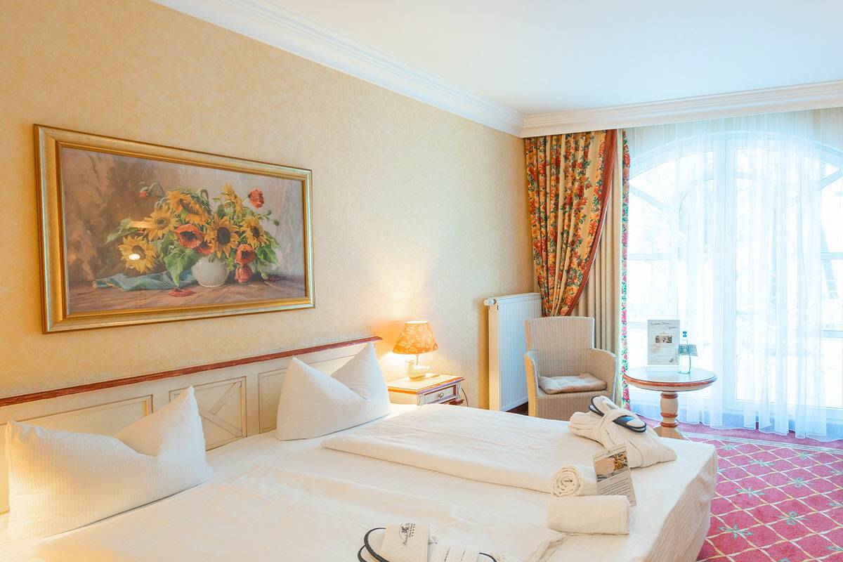 Gemütliches Hotelzimmer mit Doppelbett, in der Ecke ein Sessel und ein Bild an der Wand.