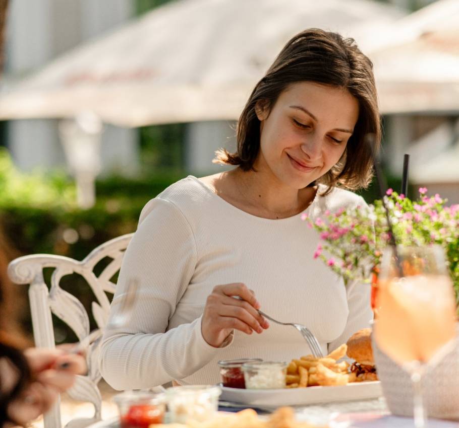 Frau genießt bei Sonnenschein ein Mittagessen mit Pommes, Burger und Getränk im Freien auf Rügen.