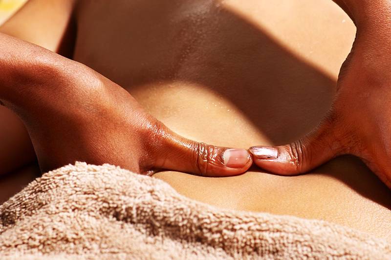 Nahaufnahmen der Hände eines Wellness-Mitarbeiters, der eine Ganzkörpermassage mit aromatischem Öl durchführt und dabei den Rücken massiert.