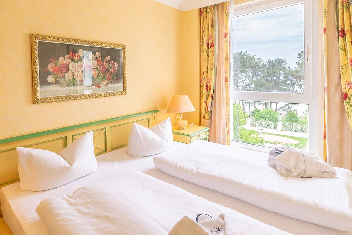 Ein gemütliches Hotelbett vor einem Fenster mit Blick aufs Meer