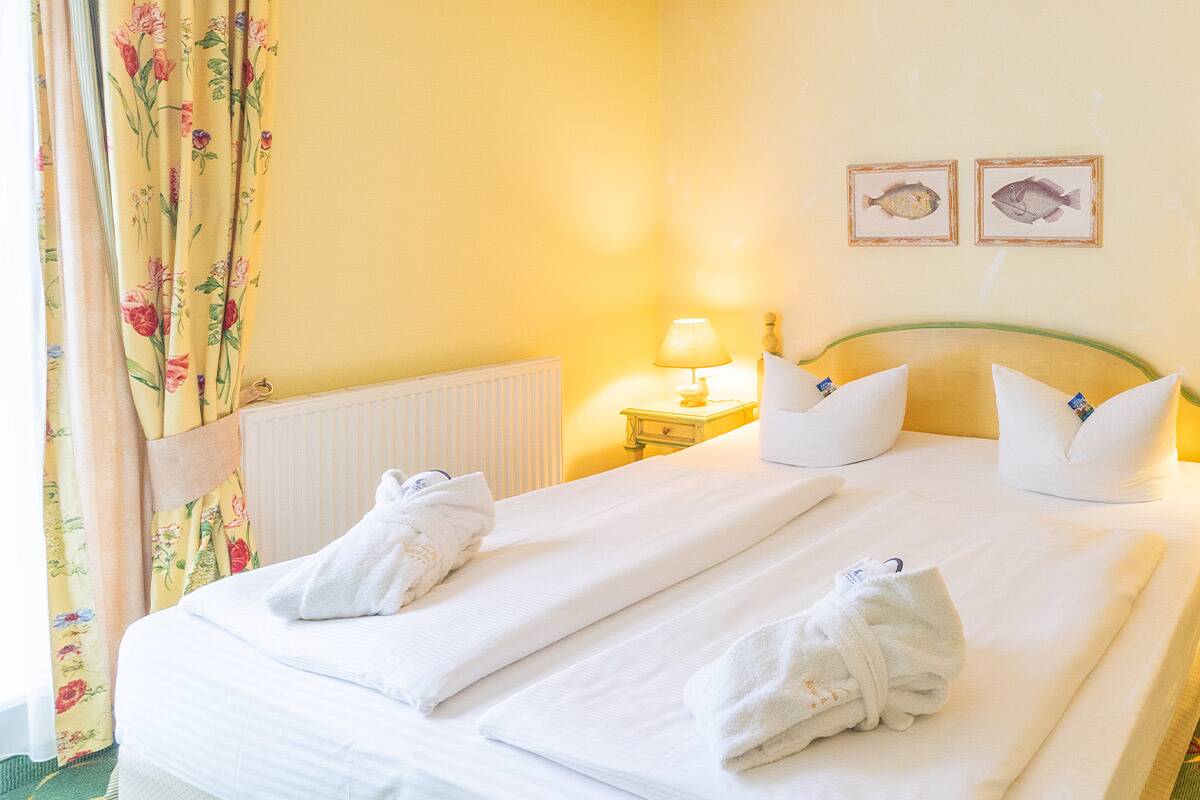 Grün und gelbes Hotelzimmer mit Doppelbett, an der Wand zwei Bilder von Fischen.