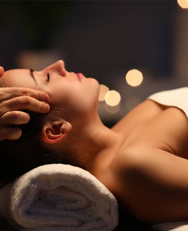 Eine Dame liegt entspannt auf einer Liege und bekommt eine Kopfmassage.