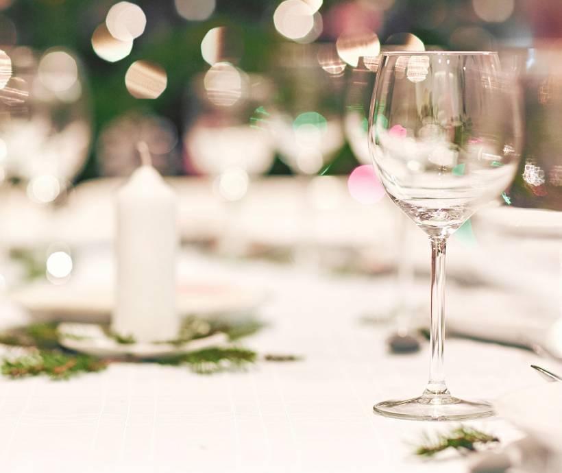 Ein leeres Glas steht auf einem weiß gedeckten Tisch mit Adventsschmuck und einer weißen Kerze.