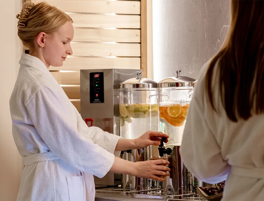 Woman in a bathrobe taps fresh Rügen water with citrus fruits at the spa bar of the Rugard Thermal Strandhotel.