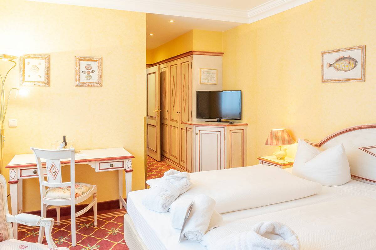Elegantes gelbes Hotelzimmer mit Doppelbett, an der Wand ein Schreibtisch.