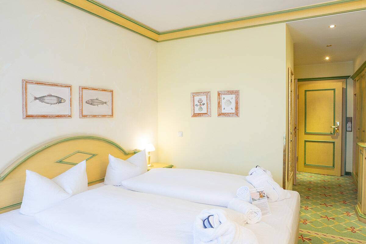 Doppelzimmer mit großem Bett, gelben und grünen Details und Teppichboden.