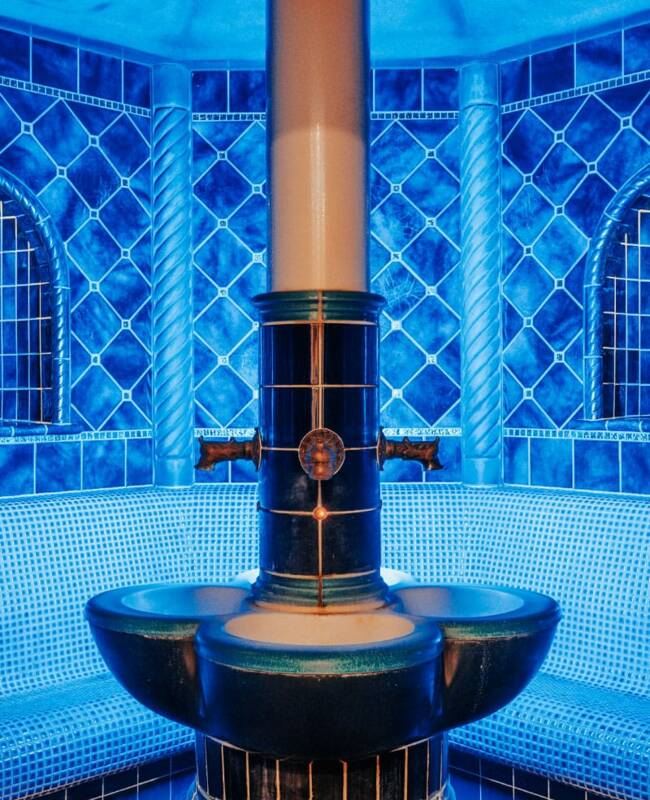 Dampfbad mit einer Säule in der Mitte, mit blauen Fließen und Wandverzierungen. im Wellness Rugard Strandhotel auf Rügen.