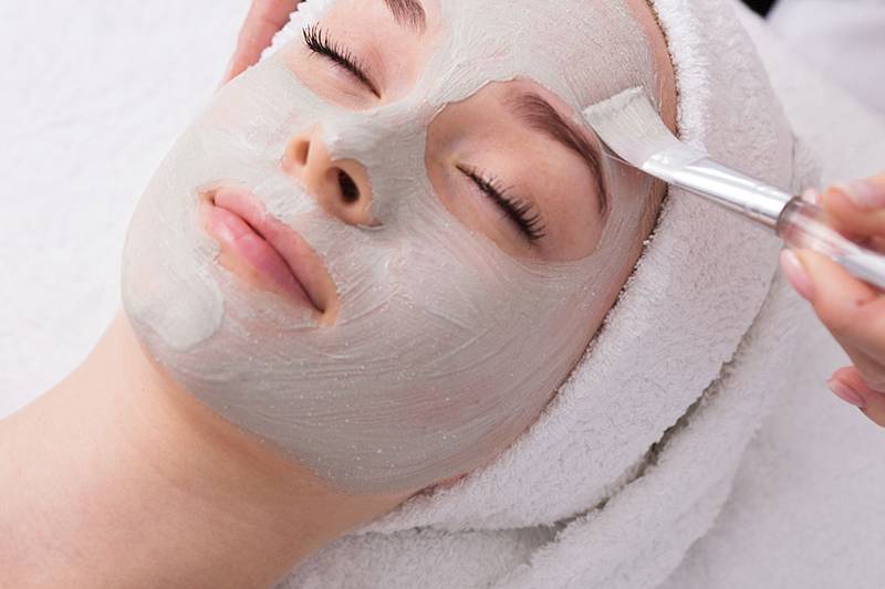 Eine graue Gesichtsmaske von Biodroga wird sanft bei einer Frau aufgetragen.