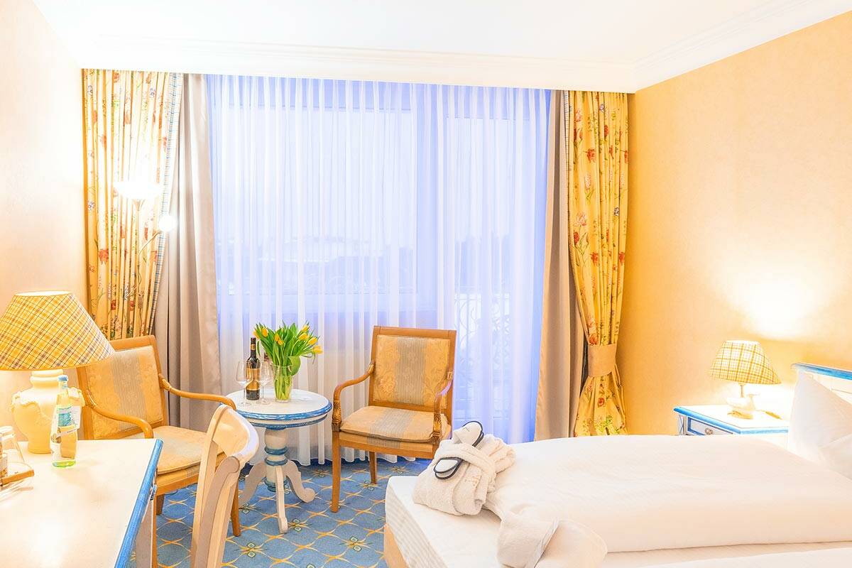 Doppelzimmer mit großem Bett, gelben und grünen Details und Teppichboden.