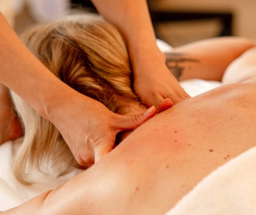 Rückenmassage bei einer Frau mit blonden Haaren, Nahaufnahme der massierenden Hände im Wellnessbereich.
