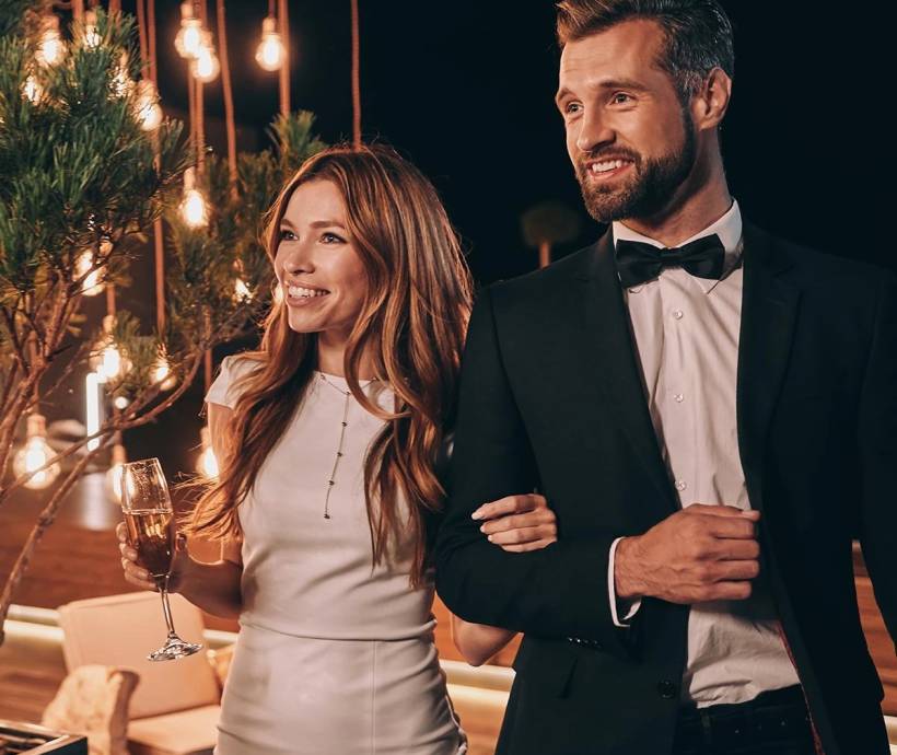 An elegantly dressed, smiling couple enters an event.