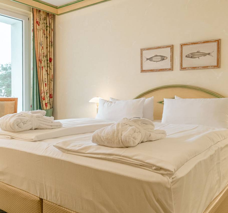 Doppelbett in der Junior Suite des Rugard Strandhotels mit zwei Bademänteln und Blick aus dem Fenster auf die Ostsee