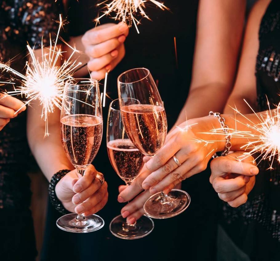 Three people, with only their hands visible, toast with champagne glasses and sparklers.