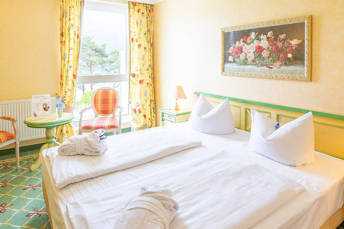 Hotelzimmer im Landhausstil mit Doppelbett, Tisch und Stühlen, an der Wand ein Bild.