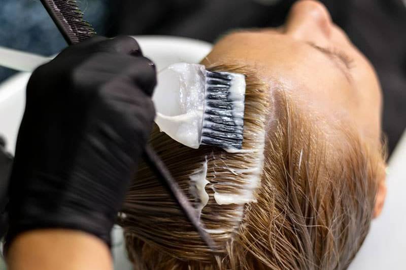 Auftrag neuer Haarfarbe mit dem Pinsel auf dem Haar einer Kundin.