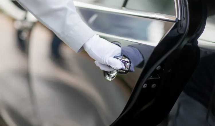 Close-up of the gloved hand of a hotel employee opening a dark car door.