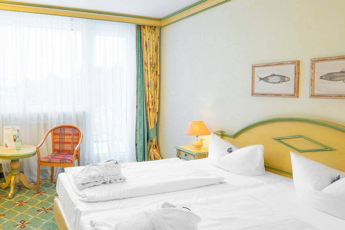 Hotelzimmer im Landhausstil mit Doppelbett, Tisch und Stühlen, an der Wand hängen zwei Bilder.