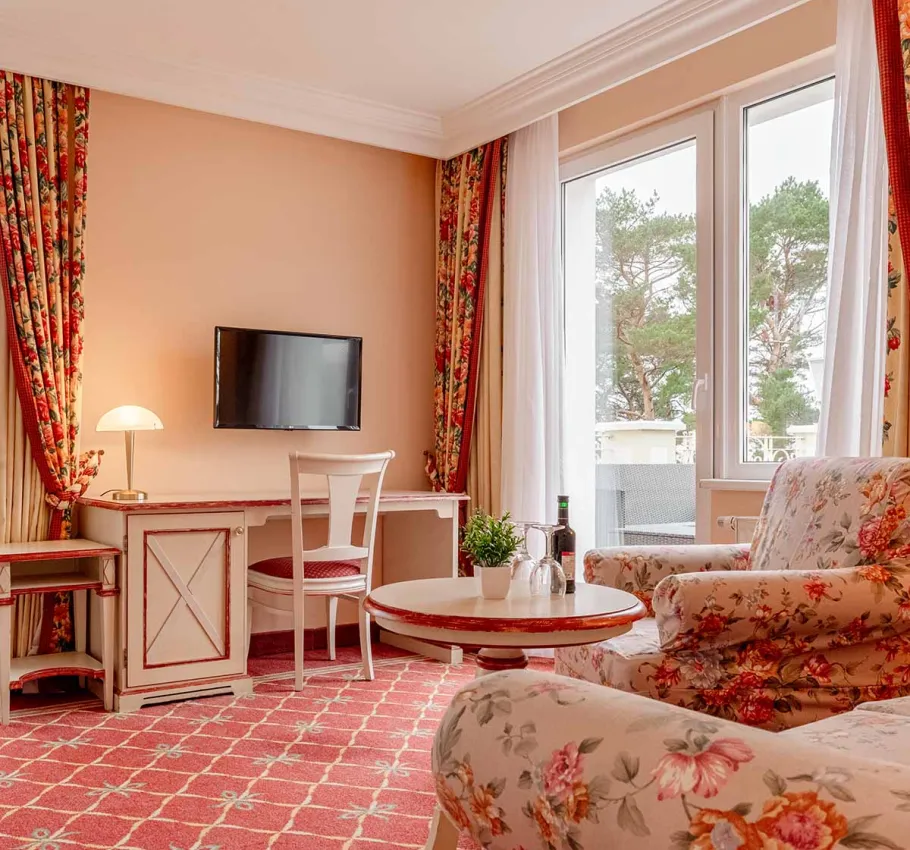 Eine gemütliche Sitzecke mit floralen Sesseln, rundem Tisch und einem Blick auf die Terrasse der Suite zur Meerseite im Rugard Strandhotel Binz.