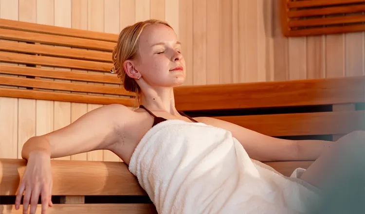 Young woman in a white towel sits with her eyes closed in the sauna at the Rugard Thermal Strandhotel.