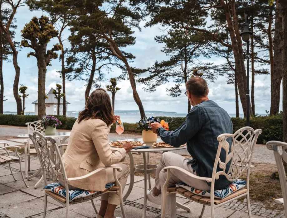 Paar genießt Speisen und Getränke auf der Terrasse des Rugard Strandhotels in Binz mit Blick auf die Ostsee.