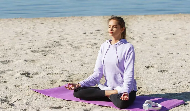 Woman meditating during yoga on the beach on Rügen with the Baltic Sea in the background on vacation at the Rugard Thermal Strandhhotel.