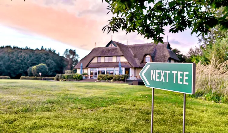 Exterior view of the golf center at sunset. In the foreground, a sign points to the next tee.