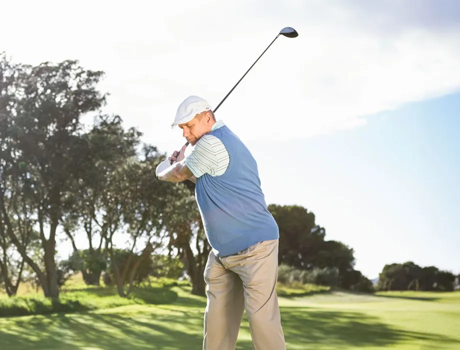 A golfer tees off, with a sunny golf course in the background.