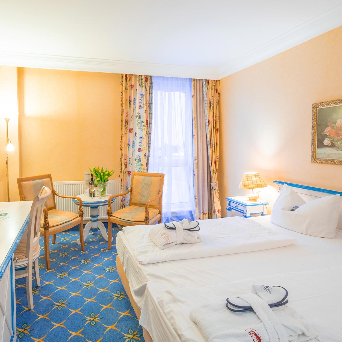 Blau und gelb dekoriertes Hotelzimmer mit Bett, Stühlen und Schreibtisch.