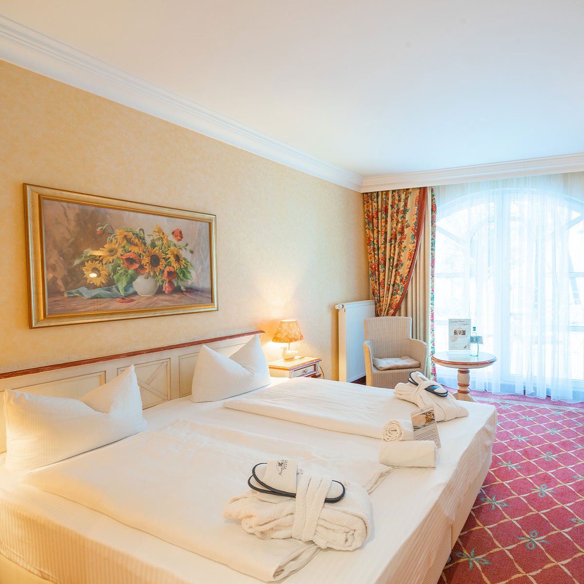Gemütliches Hotelzimmer mit Doppelbett, in der Ecke ein Sessel und ein Bild an der Wand.