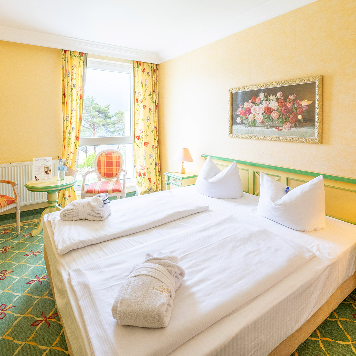Hotelzimmer im Landhausstil mit Doppelbett, Tisch und Stühlen, an der Wand ein Bild.