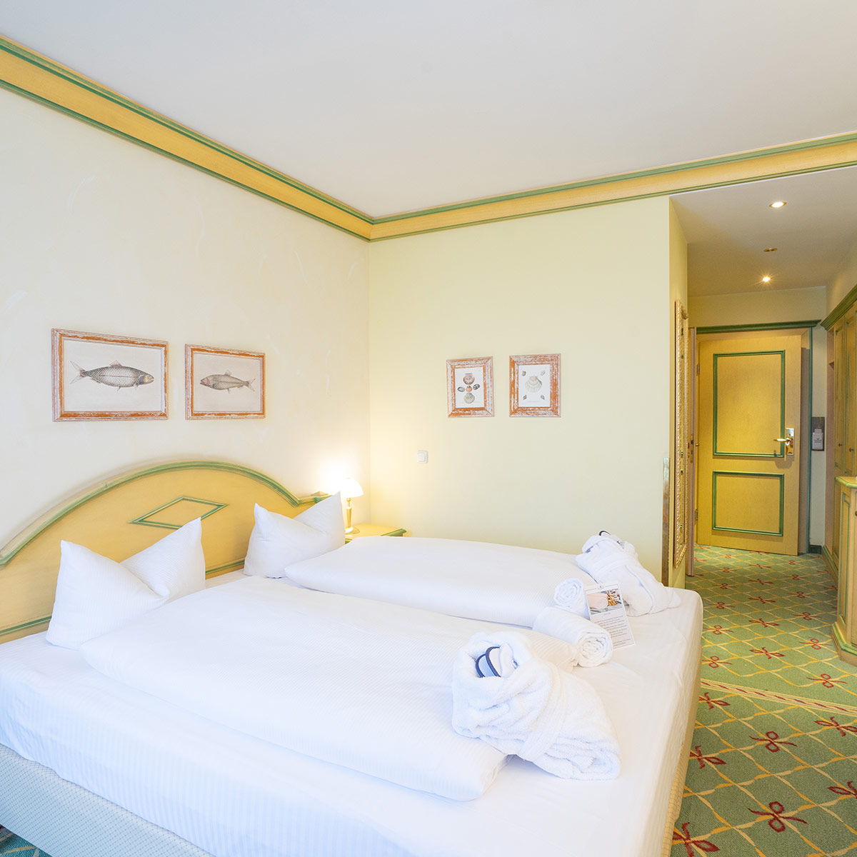 Doppelzimmer mit großem Bett, gelben und grünen Details und Teppichboden.