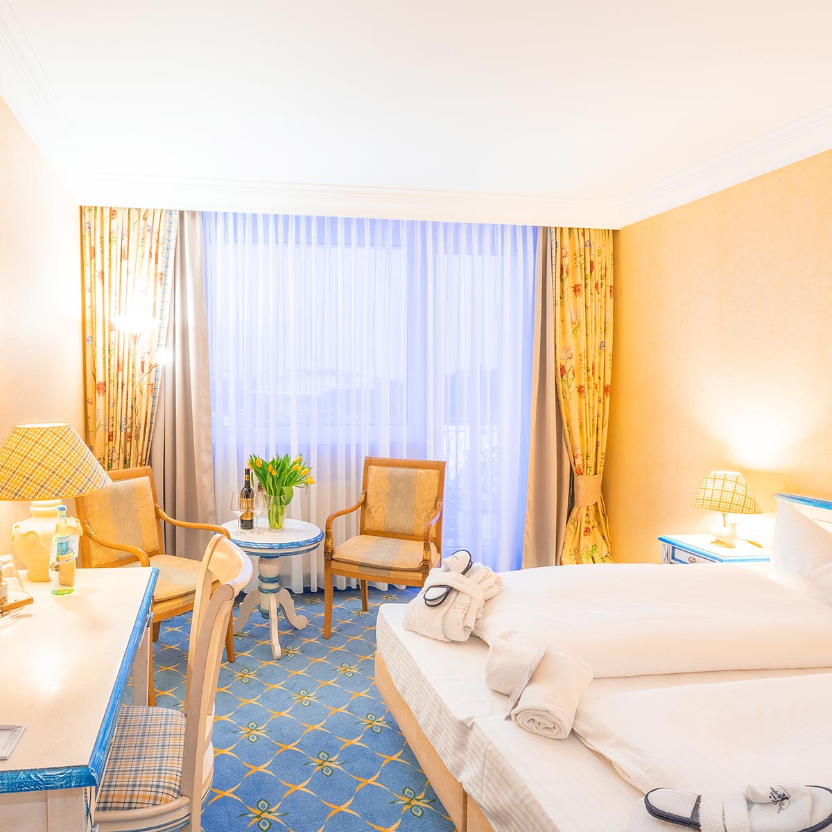 Doppelzimmer mit großem Bett, gelben und grünen Details und Teppichboden.