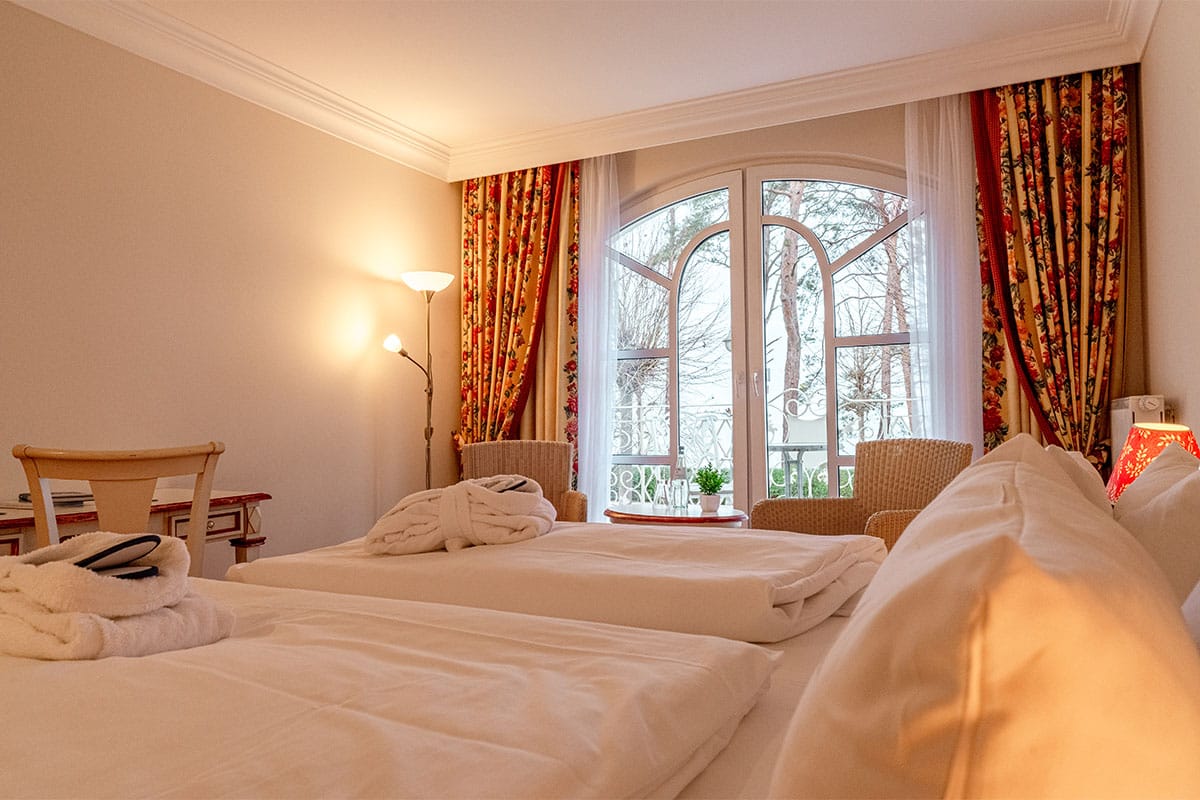 Doppelzimmer mit hellem Design, Doppelbett, Balkonblick und gemütlicher Beleuchtung im Rugard Thermal Strandhotel